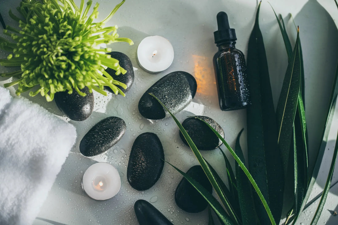 Composizione flat lay con oli naturali per la skincare, candele accese, pietre e piante, simbolo di una beauty routine serale rilassante e rigenerante